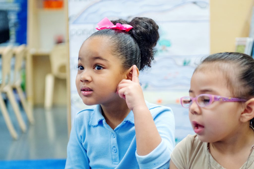 A Prek student listens to instrument sounds in kindergarten class, one of the many ways group musical play builds aesthetic awareness.
