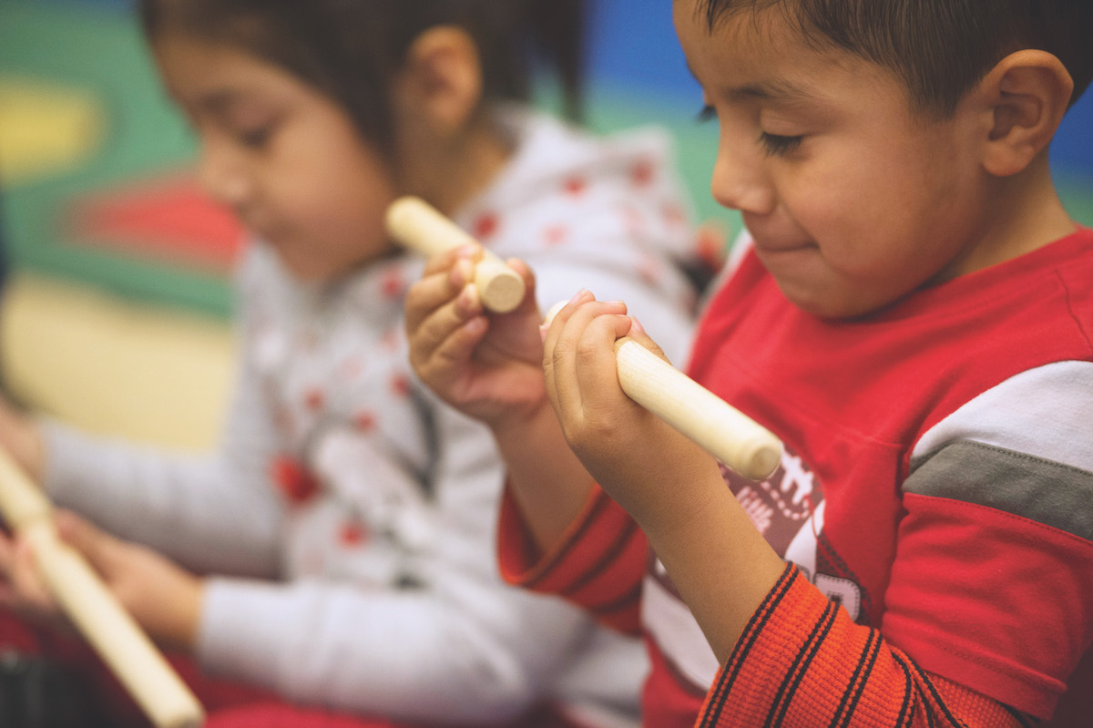 An older toddler enhances early math skills in Kindermusik class by playing with rhythm sticks.