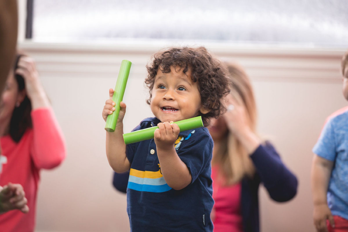 A 2-year-old boy prepares to play the fiddle sticks in a Kindermusik class.