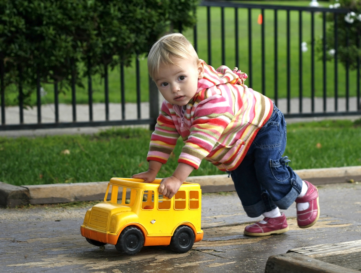 Young toddler pushes toy school bus outside.