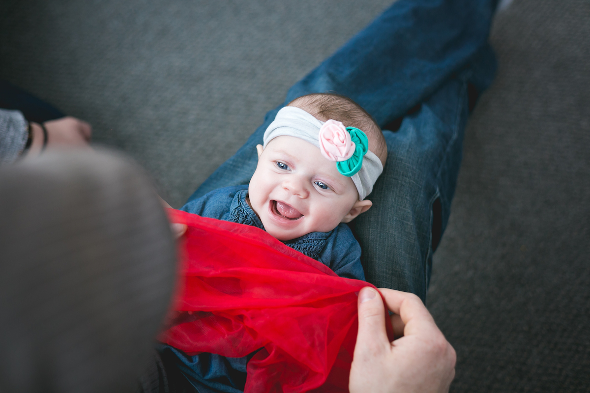 Dad plays peekaboo using sheer scarf with 6-month-old baby girl during a Kindermusik class. This example of scarf play demonstrates object permanence.
