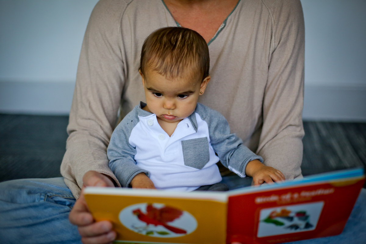 Dad boosts early reading skills by reading a board book to his baby.