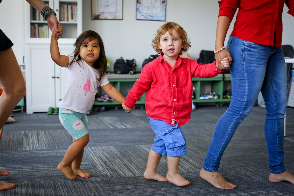 Children hold hands in a circle dance during a music class for toddlers.
