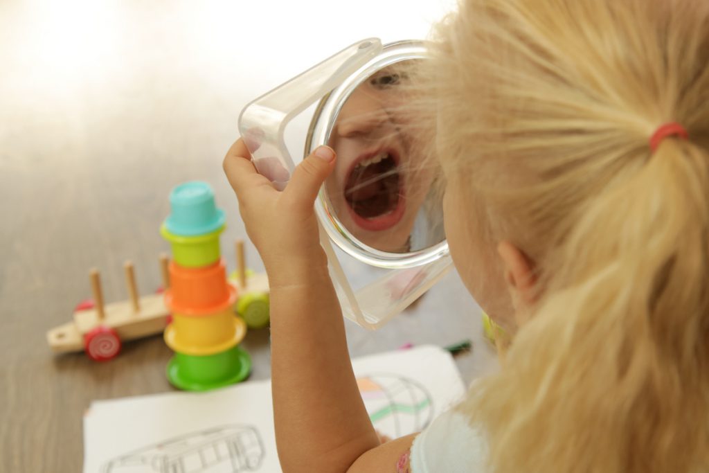 3-year-old enhances phonemic awareness by making mouth shapes with a mirror.