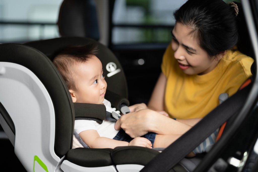 A mom sings to her baby while buckling him in the carseat, which is a great way to reduce stress and build grownup social-emotional growth.