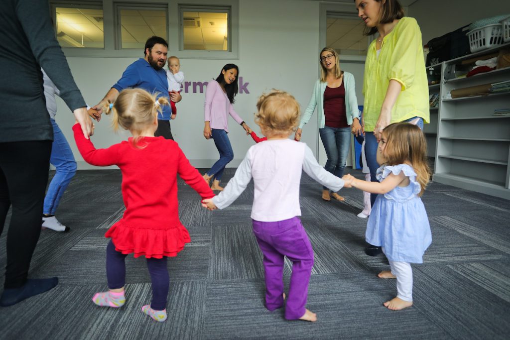 Children participate in circle dancing at a Kindermusik class, which is a great tools for synching neurodivergent learners with friends and caregivers.