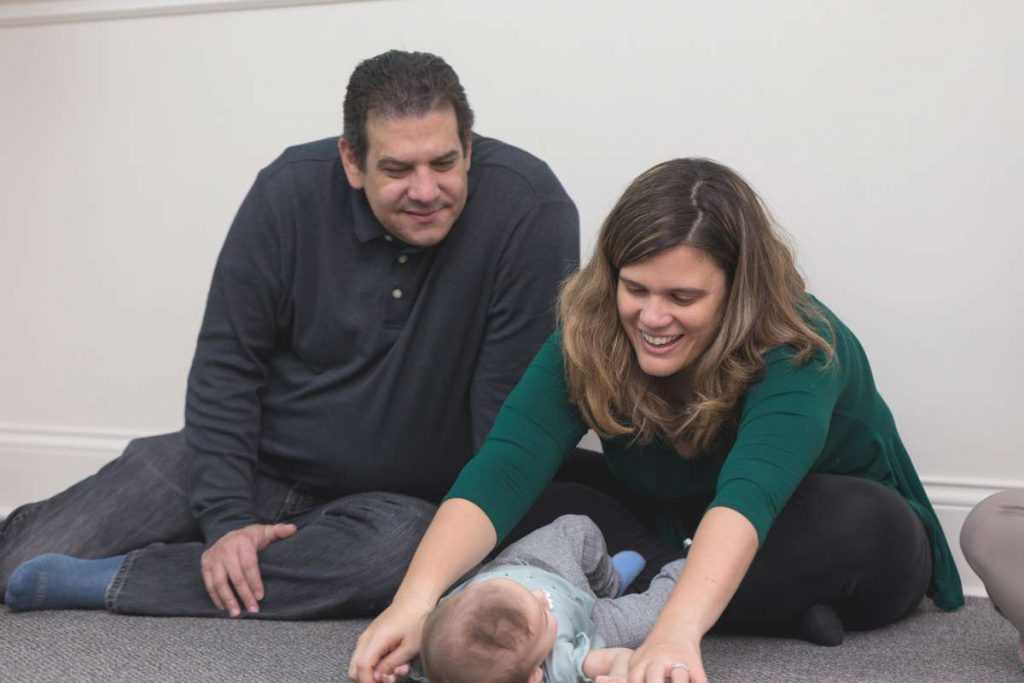 Mom and dad sit on floor and sing to baby on mat to promote secure attachment