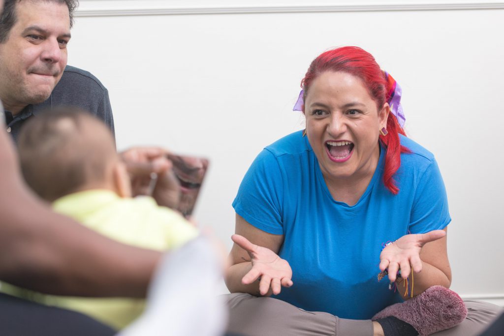 A Kindermusik teacher sings with a family and toddler as they look at mouth movements in the mirror.