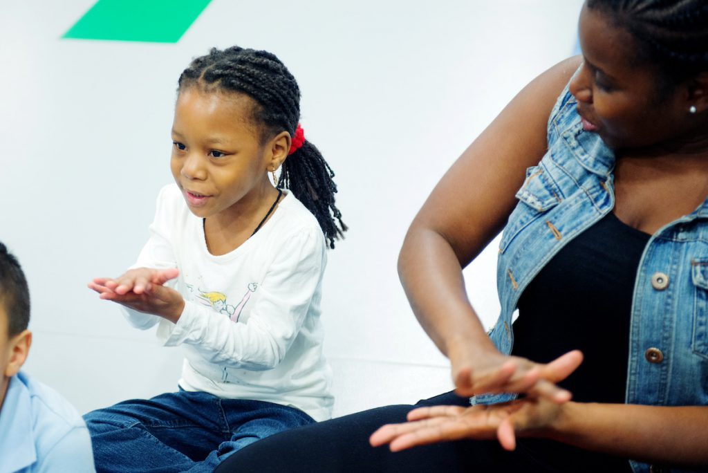 A preschool girl claps along to the music during circle time. Clapping diagonally or top to bottom can support stronger handwriting abilities.