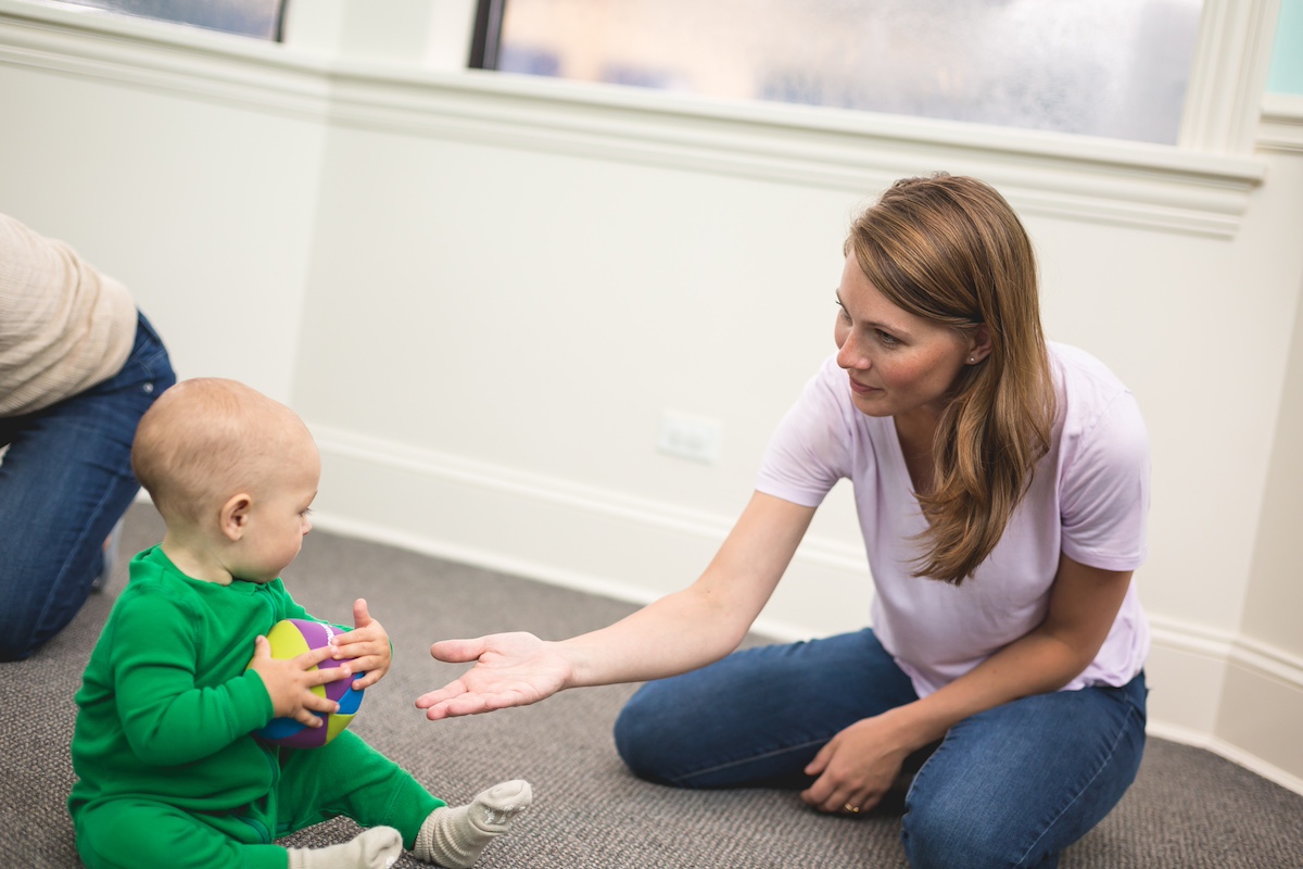 A mom passes a chime ball to her 7-month-old son during a Kindermusik class serve and return activity.