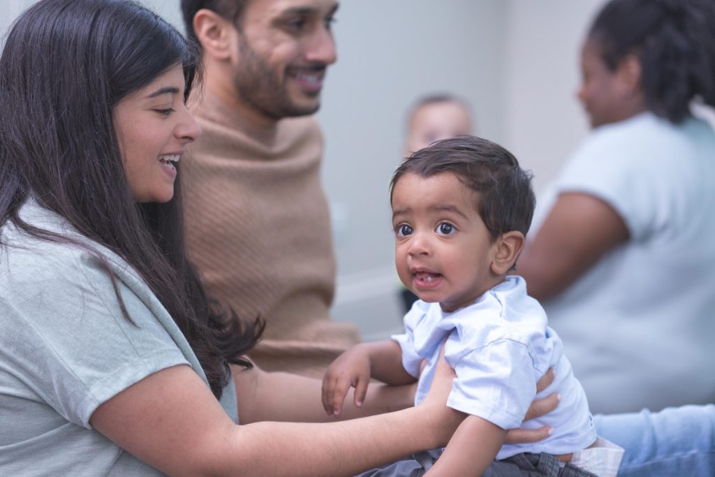 A mom bounces her 11-month-old son on her lap during a Kindermusik class; the interpersonal synchrony that happens during lap bounces supports early emotional intelligence.